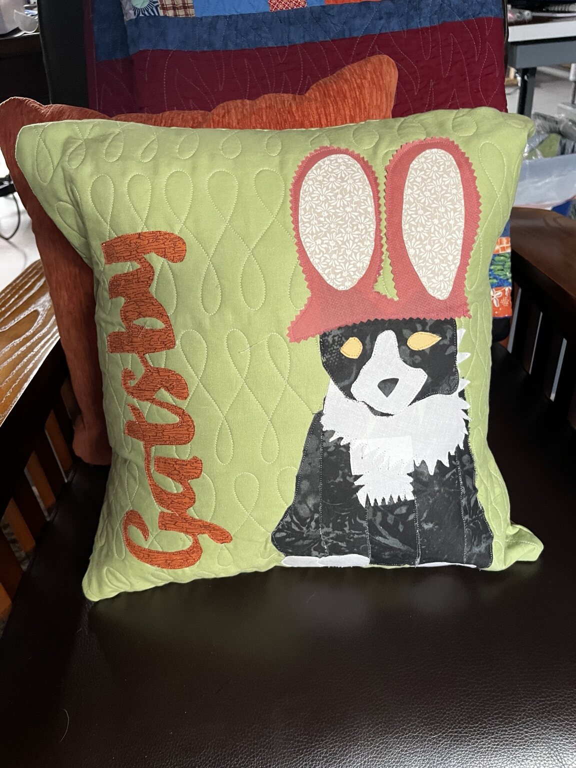 Personalized green quilted pillow featuring a black-and-white cat in a pink bunny hat